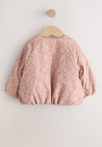 Chaqueta rosa de manga larga para niño pequeño con pequeño estampado floral colgada en un perchero de madera sobre un fondo blanco.