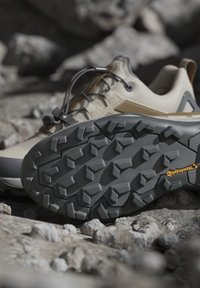 Scarpa da trekking in tonalità beige e marrone con suola in gomma nera Continental che mostra un modello di battistrada aggressivo su terreno roccioso.