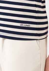 Námořnické modro-krémové pruhované tričko s krátkými rukávy, se štítkem na bočním lemu s nápisem "LES LUNES." Bavlněná směs s jemnou texturou.