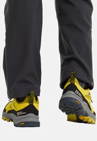 Scarpe da trail con un design nero e giallo. Presentano un materiale superiore texturizzato, una suola ammortizzata e una suola Vibram per la trazione.