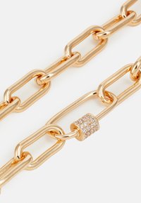 Goldfarbener Kettenanhänger mit Gliederdesign, glatter Oberfläche und einem dekorativen, mit Kristallen besetzten runden Verschluss in der Mitte.