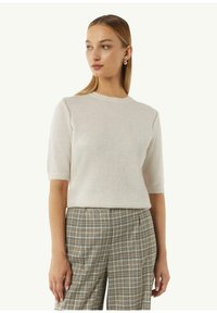 Helles beiges Kurzarm-Pullover mit rundem Halsausschnitt, der eine weiche Textur und dezente Stichdetails aufweist, kombiniert mit karierter Hose.