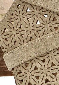 Sandalia de ante beige con diseño floral recortado en las correas, detalles cosidos y un tacón de madera para añadir textura.