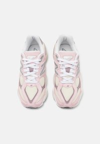 Sapatilhas rosa claro com detalhes em branco e cinza. Materiais de malha e camurça formam a parte superior. Apresentam atacadores brancos e um colarinho almofadado.