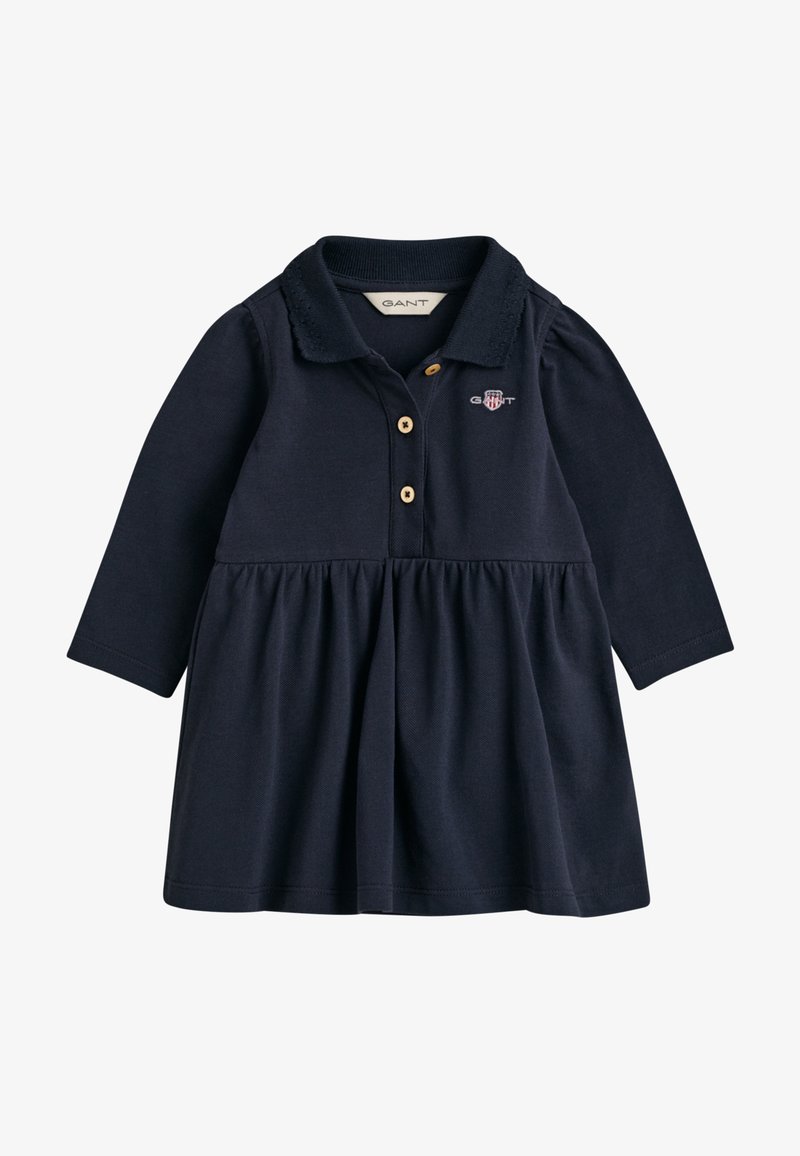 Námořnické modré šaty s dlouhými rukávy, polo límečkem, zapínáním na knoflíky, nařasenou sukní a vyšívaným logem na hrudi. Měkký bavlněný materiál.