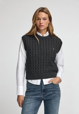 Gilet sans manches en tricot gris avec un ourlet côtelé, superposé à une chemise blanche à col, associé à un jean bleu.