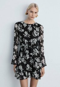 Black floral dress in lightweight fabric, featuring long sleeves, a cinched waist with a tie, and a ruffled hemline with a white flower pattern.