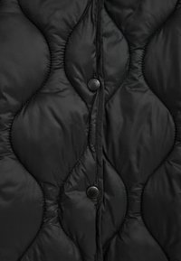 Zbliżenie na czarną pikowaną tkaninę z falistym przeszyciem i dwoma matowymi czarnymi napami wzdłuż pionowego szwu.