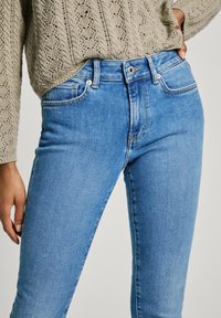 Vaqueros de algodón azul claro con forma ajustada, con un botón y remaches plateados, y un sutil efecto de desgaste para dar textura. Combinados con un suéter de punto.