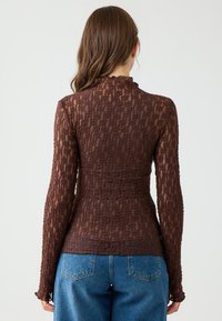Bruine getextureerde longsleeve top met een ruchesnek. Getailleerd ontwerp, elastisch materiaal, lichte rek, gecombineerd met blauwe high-waisted jeans.