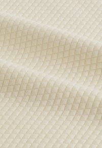 Tessuto ruvido di colore bianco sporco con un motivo a diamante, che presenta quadrati in rilievo che creano una superficie tattile e una leggera lucentezza.