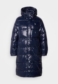Cabană puf navy blue cu finisaj lucios, glugă, închidere cu șnur și capse. Prezintă un design matlasat și buzunare laterale.