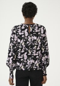 Blusa nera con motivo astratto rosa e crema, maniche lunghe a sbuffo e dettaglio a chiave sulla schiena, realizzata in un tessuto leggero.