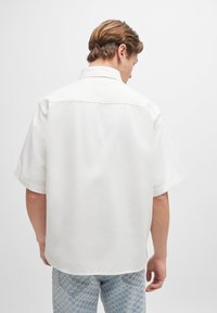 Kurze Ärmel, weißes Hemd aus Baumwolle, mit einem entspannten Schnitt, spitzem Kragen und glatter Textur. Die Rückansicht zeigt ein schlichtes Design.