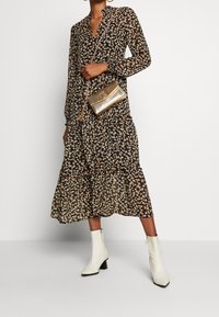 Vestido negro con flores de manga larga, diseño en capas y flores en un tono beige claro. Combinado con un bolso metálico dorado y botas blancas hasta el tobillo.