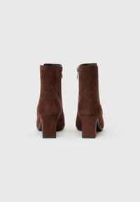 Bottines en daim marron avec un talon carré, une fermeture éclair latérale et une texture lisse. Design simple avec un empiècement légèrement plus haut.