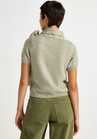 Kortärmad, ljusgrön tröja med en strukturerad krage. Mjuk textur, stickad design, ihopparad med olivgrön högmidjad byxa.