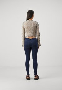 Häkelstil, langärmliger, verkürzter Pullover aus mehrfarbigem Garn, kombiniert mit dunkelblauen Skinny-Jeans und schwarzen Riemchensandalen.
