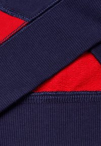 Dettaglio ravvicinato di un tessuto a coste blu navy con foderato in pile rosso visibile attraverso il dettaglio delle cuciture.