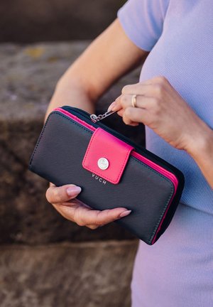Black and pink wallet with a textured finish, zip closure, and snap button detail, featuring a silver logo on the front.