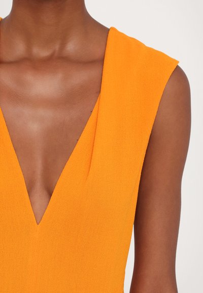 V-neck sleeveless dress in bright orange textured fabric with wide shoulder straps and a deep plunge at the neckline.