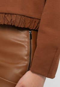 Hnědá mikina s nařaseným lemem a hladká hnědá kožená sukně s bočním zipem a elegantním vzhledem.