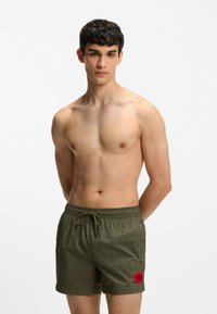 Olivgröna badshorts med elastisk midja och dragsko, med en röd rektangulär logotyp på låret.