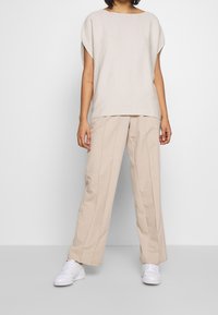 Beige kortärmad topp med vid halsringning, matchad med beige vida byxor med framfållar, kompletterad med vita sneakers.