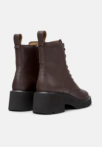 Stivali alla caviglia in pelle marrone con tacco nero spesso, dotati di un design con lacci e linguette sul retro per una facile vestibilità.