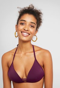 Fioletowy trójkątny stanik bikini z cienkimi ramiączkami i wycięciem z przodu. Gładka tekstura, minimalistyczny design, odpowiedni na plażę.