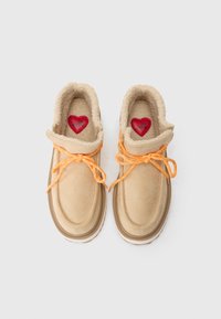 Zapatos de ante beige con cordones naranjas, forro de piel y plantilla con un corazón rojo. Punta redondeada y suela de goma gruesa, con una textura sutil.