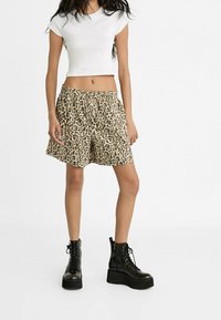 Klassisches weißes T-Shirt kombiniert mit beigen Shorts im Leopardenmuster. Das Model trägt schwarze Schnür-Plateau-Boots. Baumwollmischung, lockere Passform, elastischer Bund.