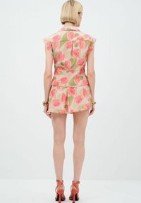 Completo floreale a due pezzi composto da top senza maniche e pantaloncini. Il materiale ha una consistenza leggera e fluida con motivi di tulipani rosa e verdi.