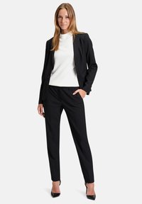 Čierna sako so dva gombíkmi, zladené nohavice na mieru a biela tričko s okrúhlym výstrihom. Modelka má na sebe čierne špicaté podpätky.