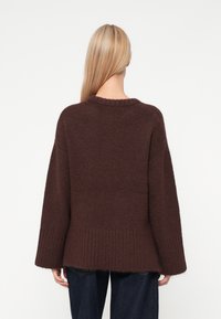 Καφέ πλεκτό πουλόβερ με χαλαρή εφαρμογή, φαρδιές μανίκες, ριμπ άκρη και στρογγυλή λαιμόκοψη. Μαλακή υφή και ελαφρώς φθαρμένες άκρες.