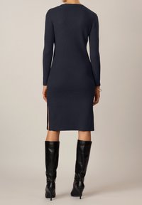 Abito in maglia rigata blu navy con maniche lunghe, caratterizzato da spacco laterale all'orlo. Abbinato a stivali neri al ginocchio.