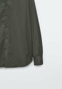 Olijfgroene blouse met lange mouwen en knopen; gemaakt van een gladde stof met groene knopen, een gebogen zoom en een klassieke kraag.