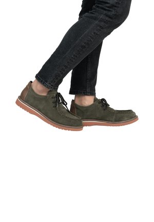 Green suede shoes with brown leather accents, lace-up design, and white stitching. The rubber sole is textured for grip. Worn with dark jeans.