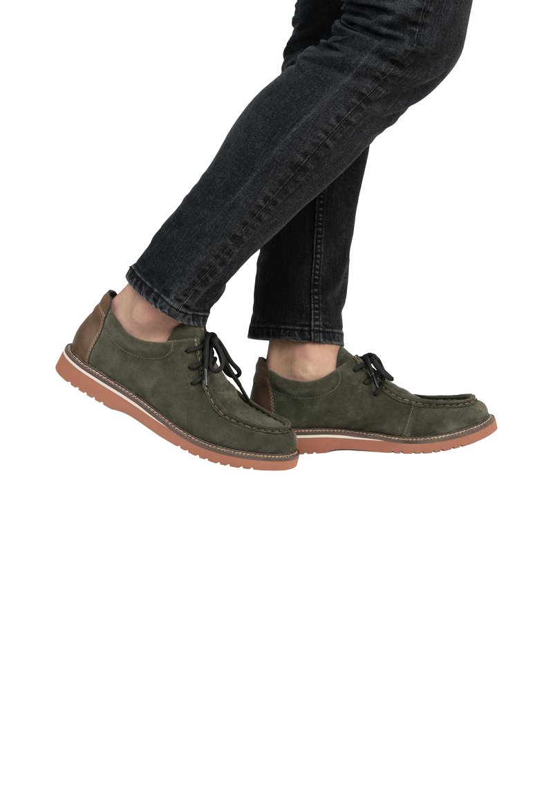 Zapatos de ante verde con detalles en cuero marrón, diseño de cordones y costuras blancas. La suela de goma tiene textura para un mejor agarre. Se llevan con jeans oscuros.