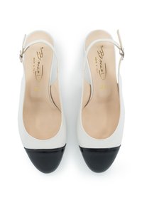 Scarpe slingback in pelle bianca con punta nera, tacco aperto e cinturino alla caviglia. Texture liscia con soletta beige contrassegnata "Made in Italy."