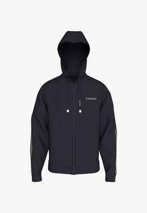 Svart hettegenser med glidelås og snorer, lite hvitt Calvin Klein-logo på brystet og diskrete gule striper på ermene.