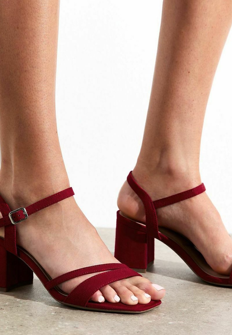 Sandali con tacco in suede rosso, dalla punta squadrata, con due sottili cinturini sulla parte superiore del piede e un cinturino alla caviglia con una fibbia metallica rettangolare.