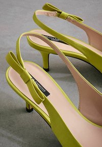 Talons slingback en daim vert avec un petit nœud, dotés d'un talon aiguille de 7,5 cm et d'une semelle intérieure beige lisse.