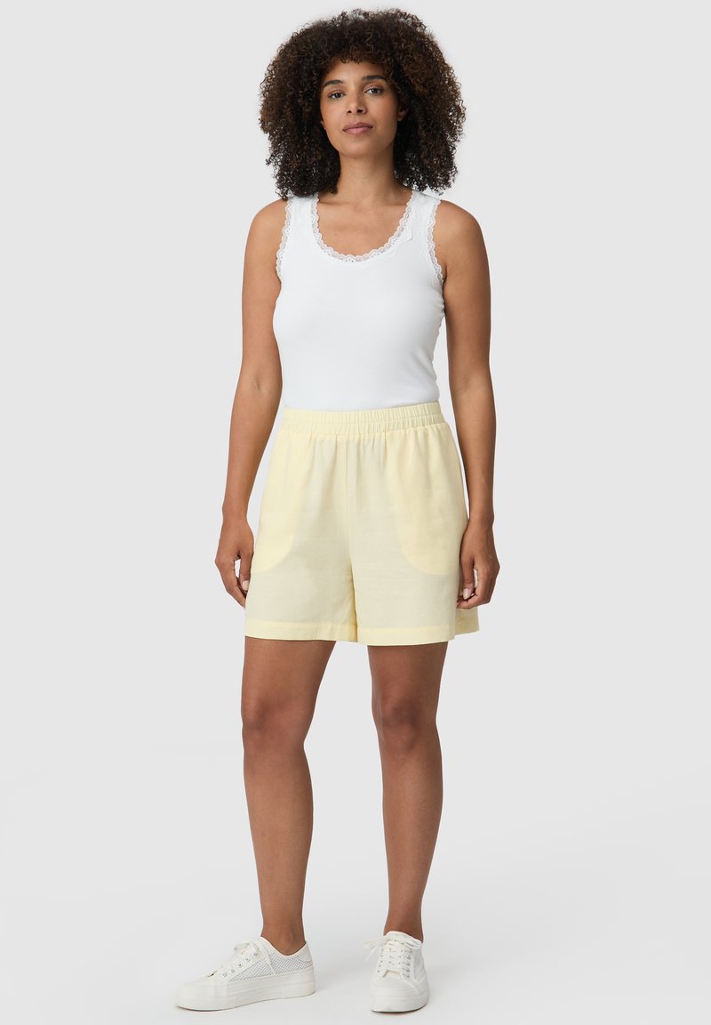 Biały top na ramiączkach z koronkowym wykończeniem, zestawiony z jasnobeżowymi szortami z elastycznym pasem i bocznymi kieszeniami. Całość dopełniają białe trampki.