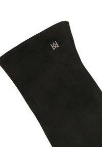 Crna zamšna čizme do koljena s glatkom teksturom i zaobljenim vrhom. Ima metalni srebrni logo akcent na gornjem dijelu.