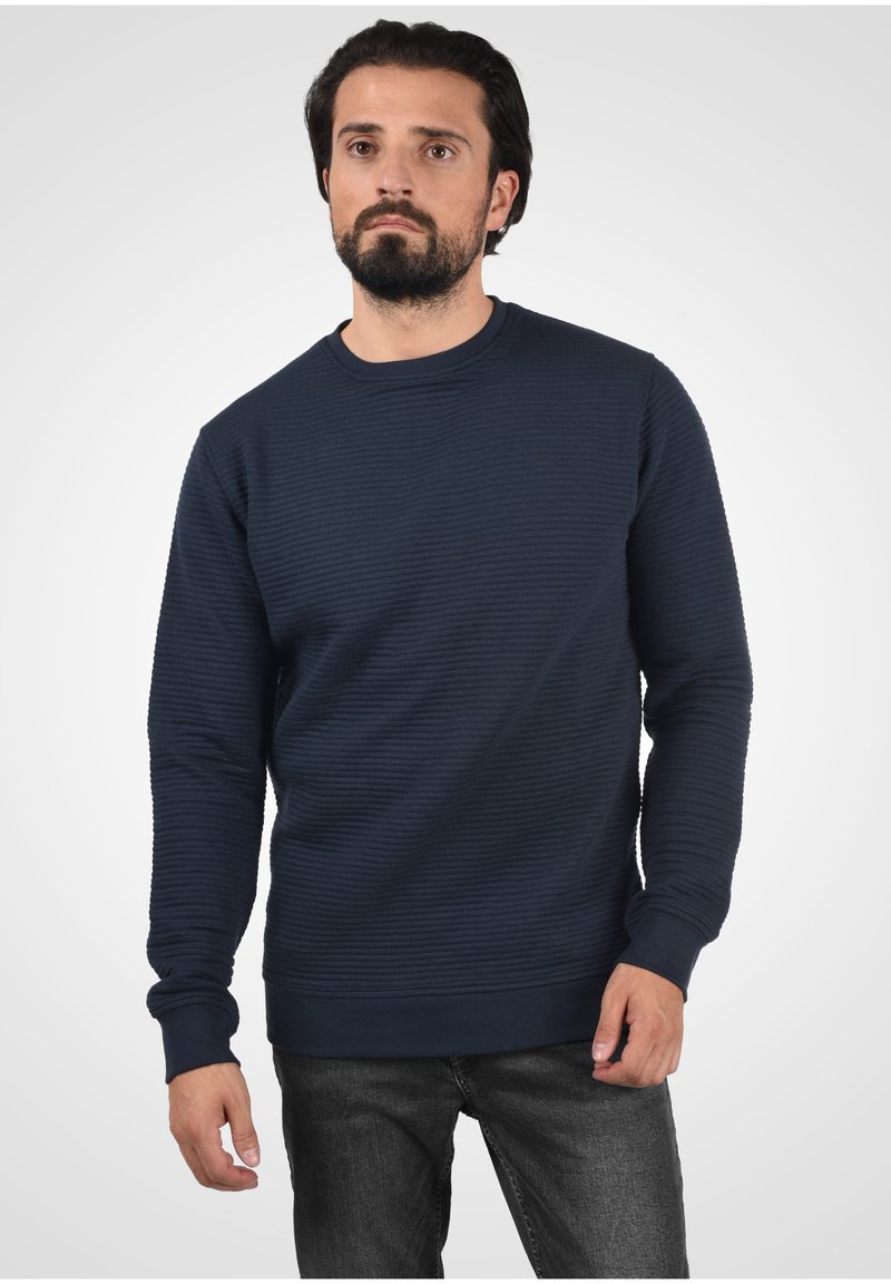 Marinblå ribbad sweatshirt i strukturerad tyg, med rundad halsringning och långa ärmar, ihop med mörka jeans.