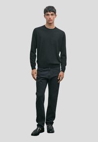 Maglione nero, jeans neri slim-fit e scarpe nere. Il maglione ha un collo a giro e maniche lunghe. Texture liscia, design minimale.
