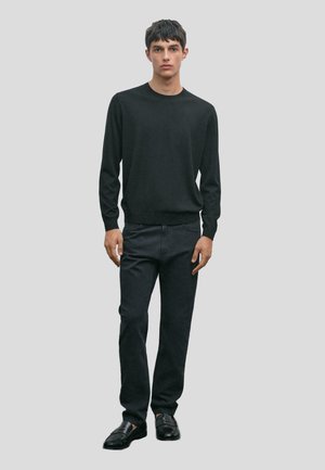 Maglione nero a maglia con maniche lunghe, abbinato a jeans scuri e mocassini neri. Design semplice, texture liscia e silhouette attillata.