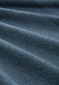 Denim-Stoff in einem tiefen Blauton, mit einer strukturierten Oberfläche, die sichtbare Webmuster und subtile Farb- sowie Tiefenunterschiede aufweist.