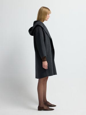 Grijze wollen jas met een grote capuchon, oversized kraag en zijzakken, gecombineerd met bruine flats en doorschijnende panty’s. Zijaanzicht.